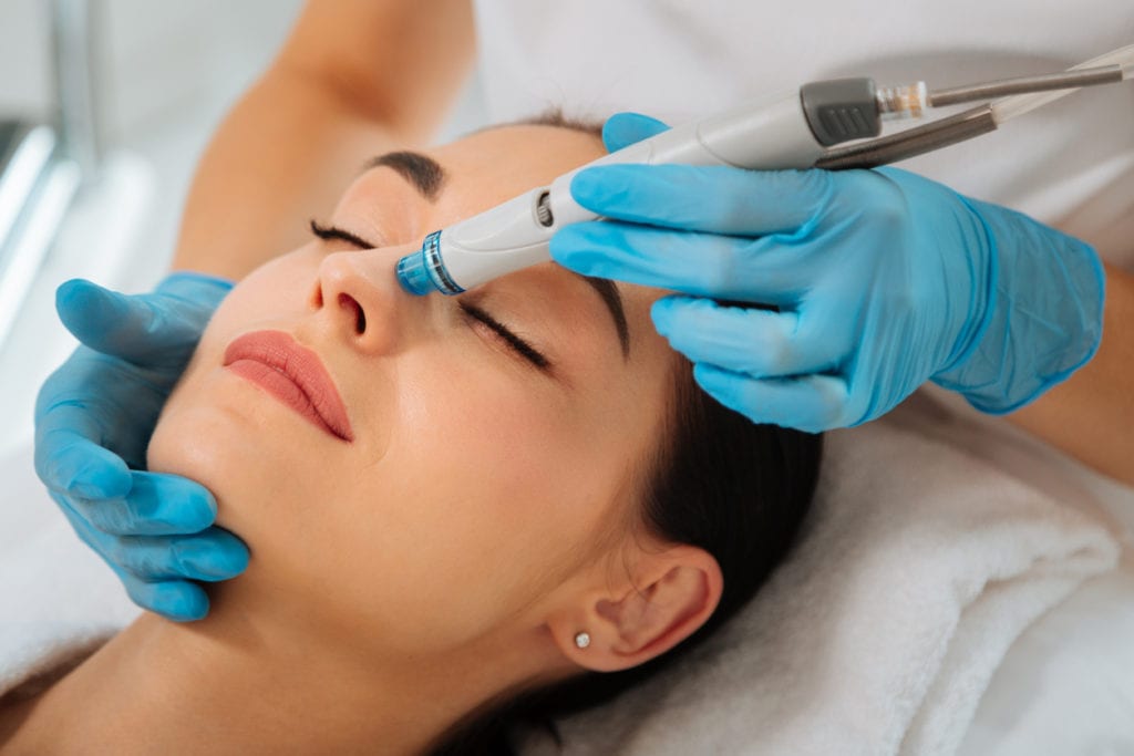 woman lying on the medical bed with her eyes closed while having hydrafacial