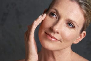 mature woman with bare shoulders looking away against a gray background - Skin Aging